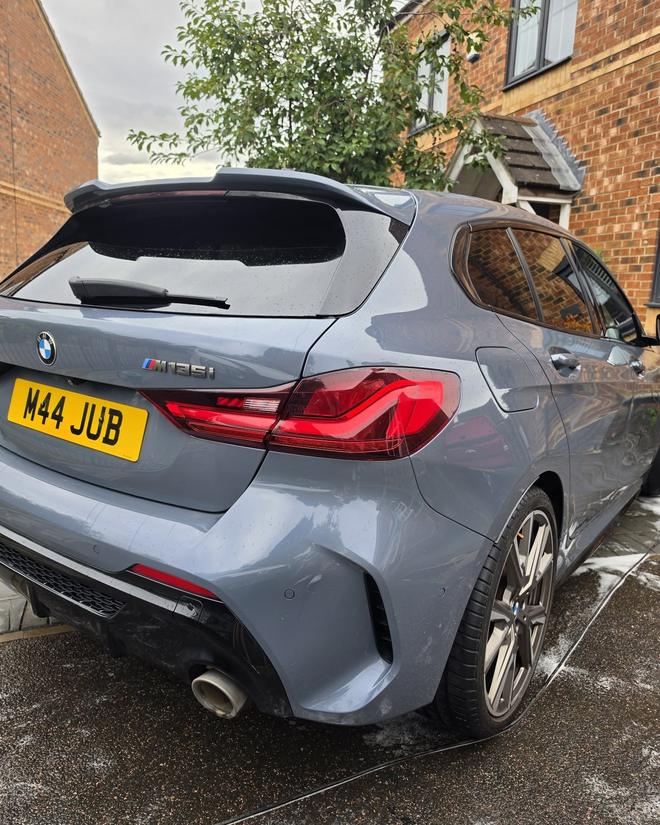 A grey BMW M135i after a wash, wet paintwork gleaming on the driveway